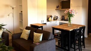 Un ambiente compatto con angolo cottura, un divano con cuscini decorati, un tavolo da pranzo con sedie e un vaso con fiori.