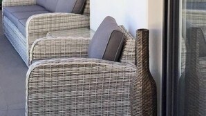 Un divano in vimini con cuscini, addossato a una parete di vetro.