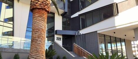 A modern building with a palm tree in the foreground, a staircase, and a number '222' on the wall.