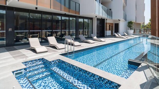 Un hotel moderno con piscina a sfioro sul tetto, lettini prendisole e facciata in vetro.