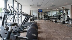 Una palestra con tapis roulant, macchinari per pesi e uno schermo televisivo.