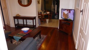 Een woonkamer met een bank, een salontafel met een schaal, een televisie op een standaard, en een eethoek op de achtergrond.