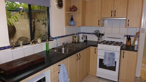Een keuken met houten kastjes, een fornuis, een gootsteen en een raam met uitzicht op groen.