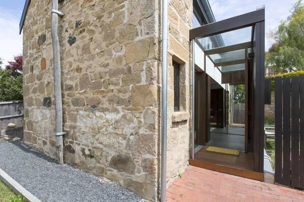 A stone building with a modern glass entrance and a metal pipe on the side.