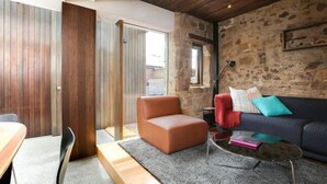 A modern living room with a stone wall, a leather sofa, a glass coffee table, and a wooden dining table.