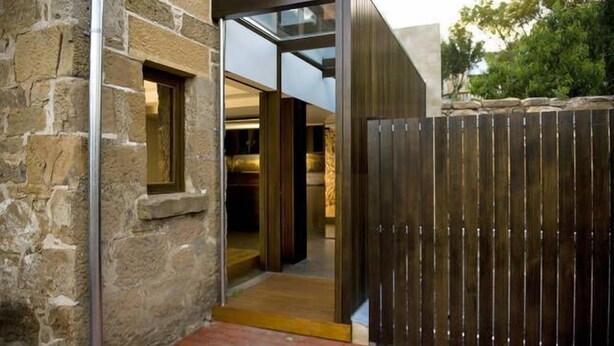 A modern building with a stone facade, a wooden fence, and a glass door leading to an interior space.
