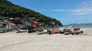 Une plage avec des bateaux aux couleurs vives, un ciel dégagé et des maisons sur une colline.