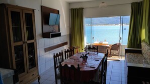 Un coin repas avec une table dressée pour six personnes, un téléviseur fixé au mur et une vue sur la mer grâce à de grandes fenêtres.