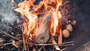 Jemand kocht Eier und Tomaten über offenem Feuer.