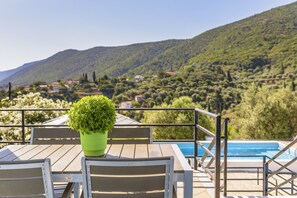 A wooden table with a potted plant, a pool, and a view of a hillside with houses. - House with character, private swimming pool, spectacular view (Samos)