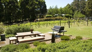 A patio with a wooden table and bench, a grill, and a small round table. - Peaceful 40-acre Gembrook Farmstay & Sanctuary - Help feed rescue animals! (Gembrook)