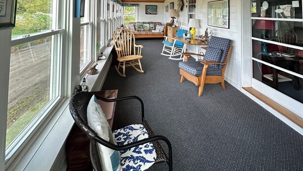 A cozy room with wooden ceiling beams, a sofa, rocking chairs, and a table with chairs.