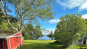 A grassy yard with a red barn and a view of a lake.