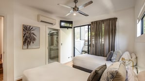 Slaapkamer met twee bedden, een plafondventilator, een airconditioning, een televisie en een groot raam met gordijnen.