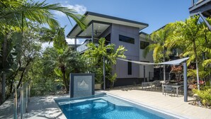 Een modern huis met zwembad, omringd door tropische planten en een terras.