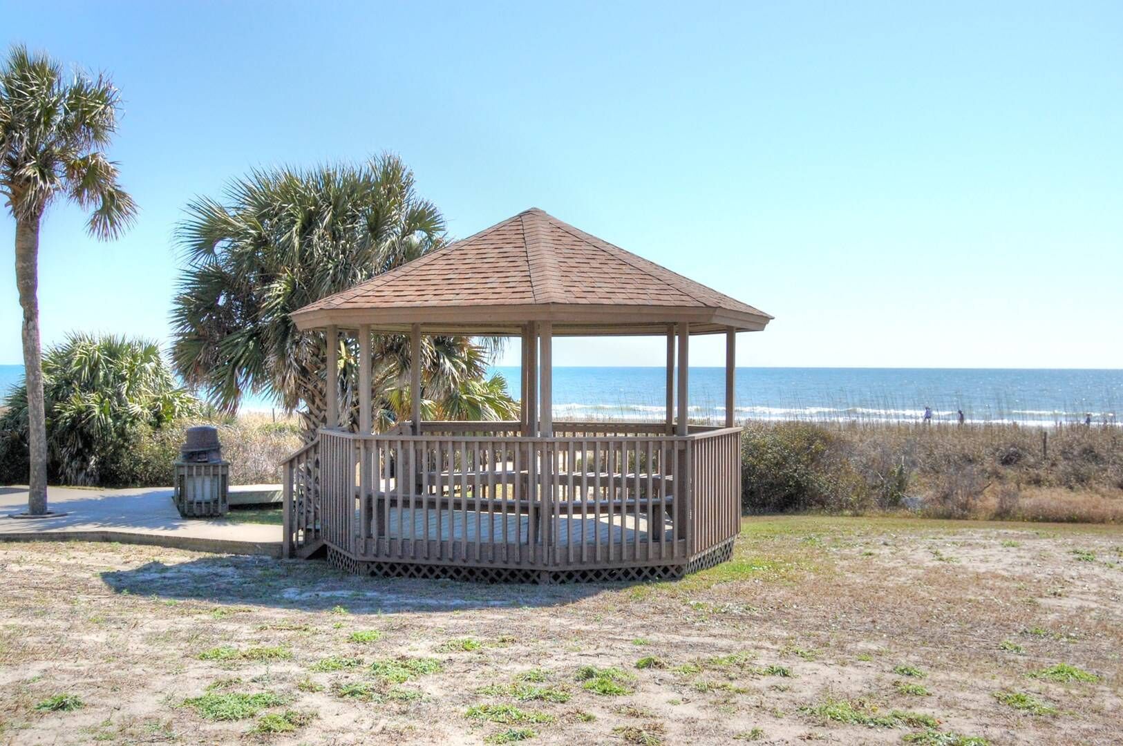 Beachside gazebo offers perfect spot for outdoor dining with stunning ocean views and tropical palm trees creating an idyllic coastal setting.