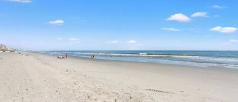 A wide sandy beach with a clear blue sky and ocean waves.