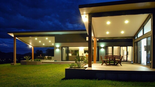 A modern house with a covered patio, a dining area, and a kitchen visible through glass doors.