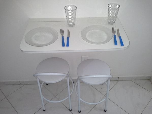Une petite table à manger avec deux assiettes, des couverts et deux verres. Deux chaises blanches sont placées devant la table.