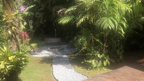 Um jardim com caminho de cascalho, deck de madeira e diversas plantas.