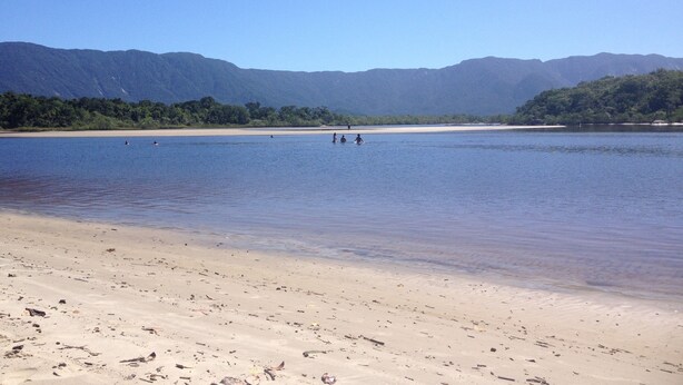Uma praia com vista clara para o mar e montanhas ao longe.