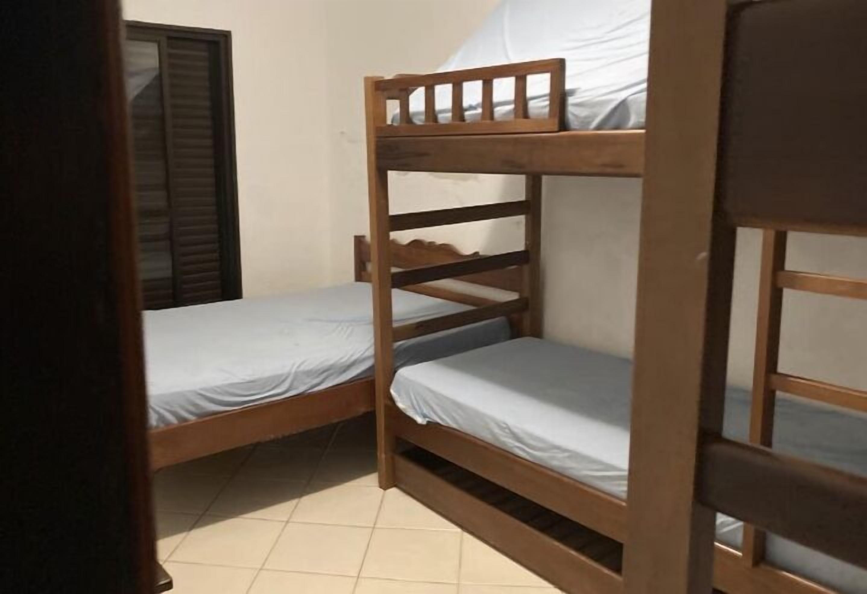 Una habitación pequeña y funcional con dos literas de madera, una ventana con persianas y piso de baldosas.