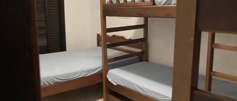 Una habitación pequeña y funcional con dos literas de madera, una ventana con persianas y piso de baldosas.