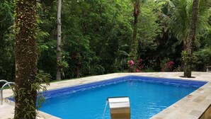 Piscina com borda em azulejo, cercada por vegetação exuberante e árvores.