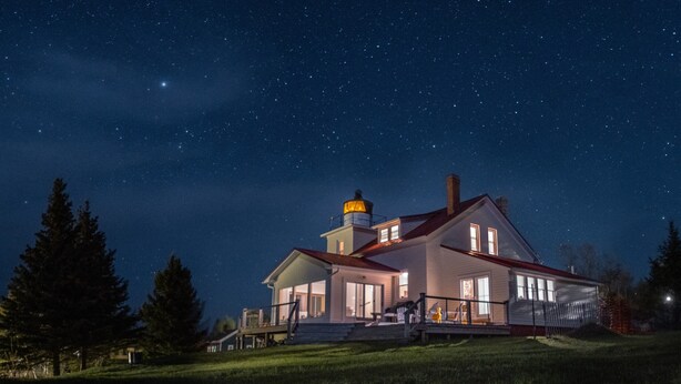 A house with a lighthouse on the roof, large windows, and a well-lit porch. - Historic 1850 Lighthouse Lake Superior (Eagle River)