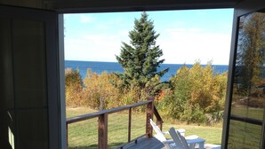 A deck with a wooden railing, a white Adirondack chair, and a black chair. - Historic 1850 Lighthouse Lake Superior (Eagle River)