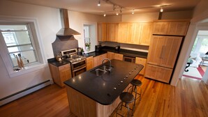 A modern kitchen with wooden cabinets, a large island with bar stools, a stove, and a built-in oven. - Historic 1850 Lighthouse Lake Superior (Eagle River)
