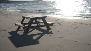 A wooden picnic table on a sandy beach with footprints around it. - Historic 1850 Lighthouse Lake Superior (Eagle River)