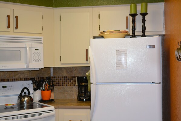 A kitchen with white appliances, including a microwave, stove, and refrigerator. There are two green candles on top of the refrigerator.