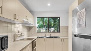 A modern kitchen with white cabinets, a stainless steel refrigerator, and a window with a view of greenery.