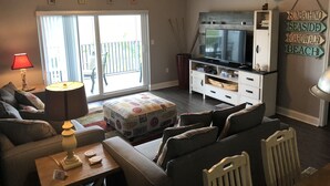 Una sala de estar con un sofá, una mesa de centro, un televisor y una estantería. Hay una puerta corrediza de vidrio que da a un balcón.