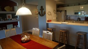 Un comedor con una mesa de madera, un mantel individual rojo y un cuenco de vidrio con aperitivos. Hay cuatro sillas de madera y una lámpara colgante.