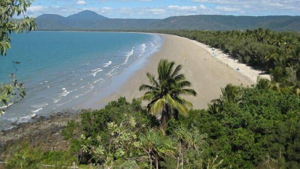 Uma praia com águas azul-claras, areal arenoso e vegetação exuberante.