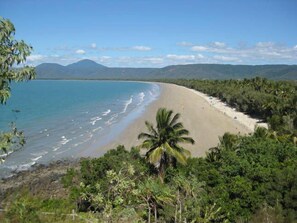 A beach with clear blue water, sandy shore, and lush greenery.