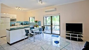 Uma cozinha moderna com uma ilha central, área de jantar com cadeiras, televisão de tela plana e uma grande porta de vidro deslizante que dá para uma área externa.