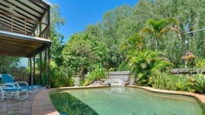 Piscina com borda curva, rodeada por um terraço de tijolos e vegetação exuberante.