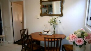 A dining area with a round wooden table, four chairs, a vase with flowers, and a mirror on the wall. - White Dog Lane Cottage Farm stay (Elleker)