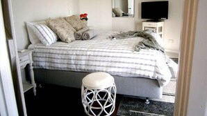 A bedroom with a bed, a bedside table, a mirror, a TV, and a small stool. - White Dog Lane Cottage Farm stay (Elleker)