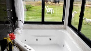 A bathroom with a large bathtub, a view of a grassy field with animals, and a white chair outside the window. - White Dog Lane Cottage Farm stay (Elleker)