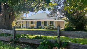 A house with a green roof, surrounded by a wooden fence and large trees. - Oaklands Homestead (Pambula)