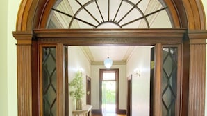 A hallway with a wooden floor, a gray rug, and a large arched doorway with glass panels. - Oaklands Homestead (Pambula)