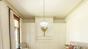 A bedroom with a large bed, a chair, a desk, and a hanging light fixture. - Oaklands Homestead (Pambula)