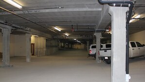 Un parking souterrain avec des piliers en béton, un éclairage fluorescent et des véhicules stationnés.