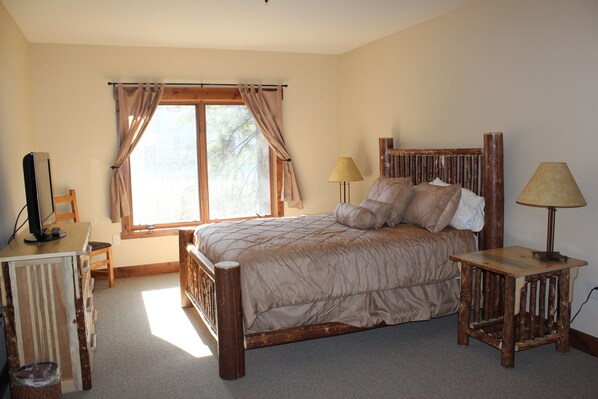 A bedroom with a wooden bed, a desk with a computer, and a window with curtains. - 3 Bedroom, 2 bathroom Condo on Big Mountain (Whitefish)