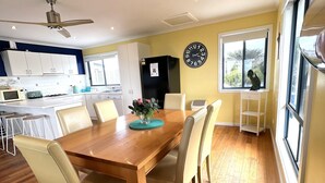 A modern kitchen with white cabinets, a black refrigerator, and a dining area with a wooden table and beige chairs.