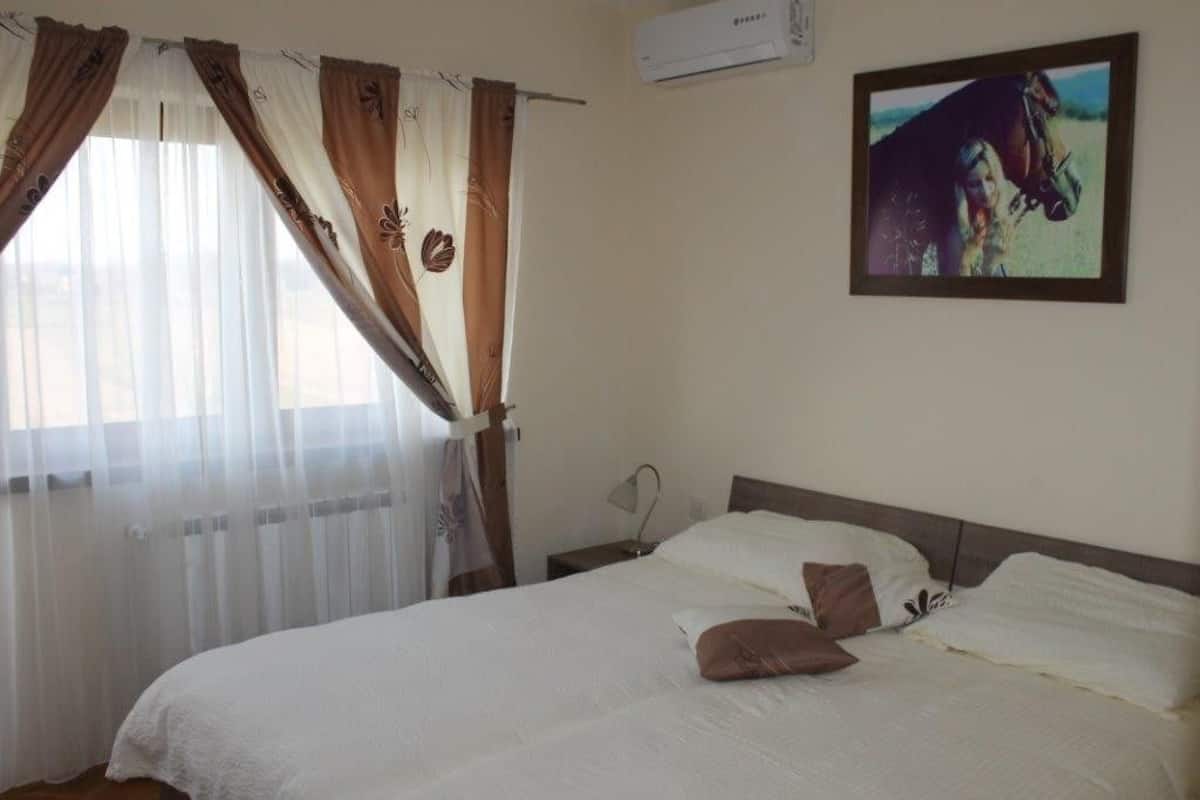 A bedroom with a bed, curtains, a wall-mounted air conditioner, and a framed picture.
